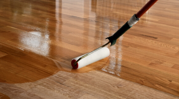 Roller applying fresh finish and stain to hardwood flooring