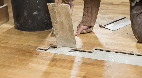 Professional applying compound to patch and repair damaged hardwood flooring