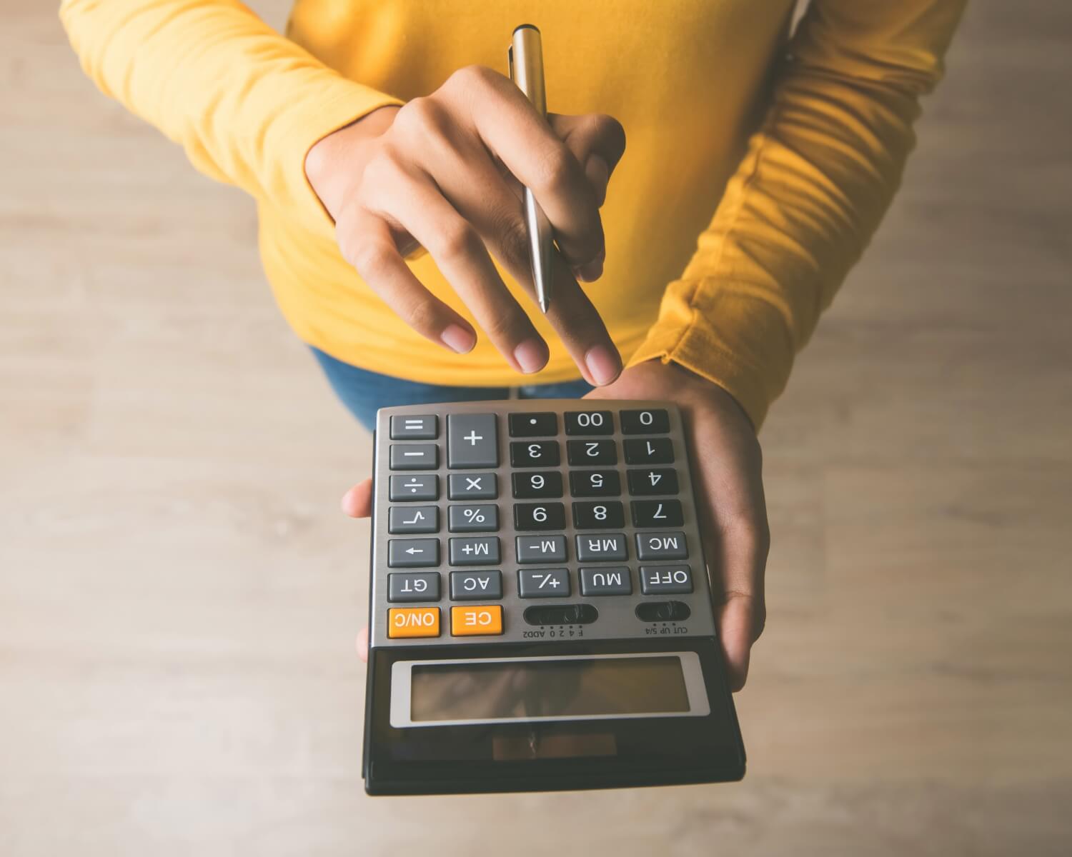 Person holding calculator with pen to estimate hardwood flooring costs